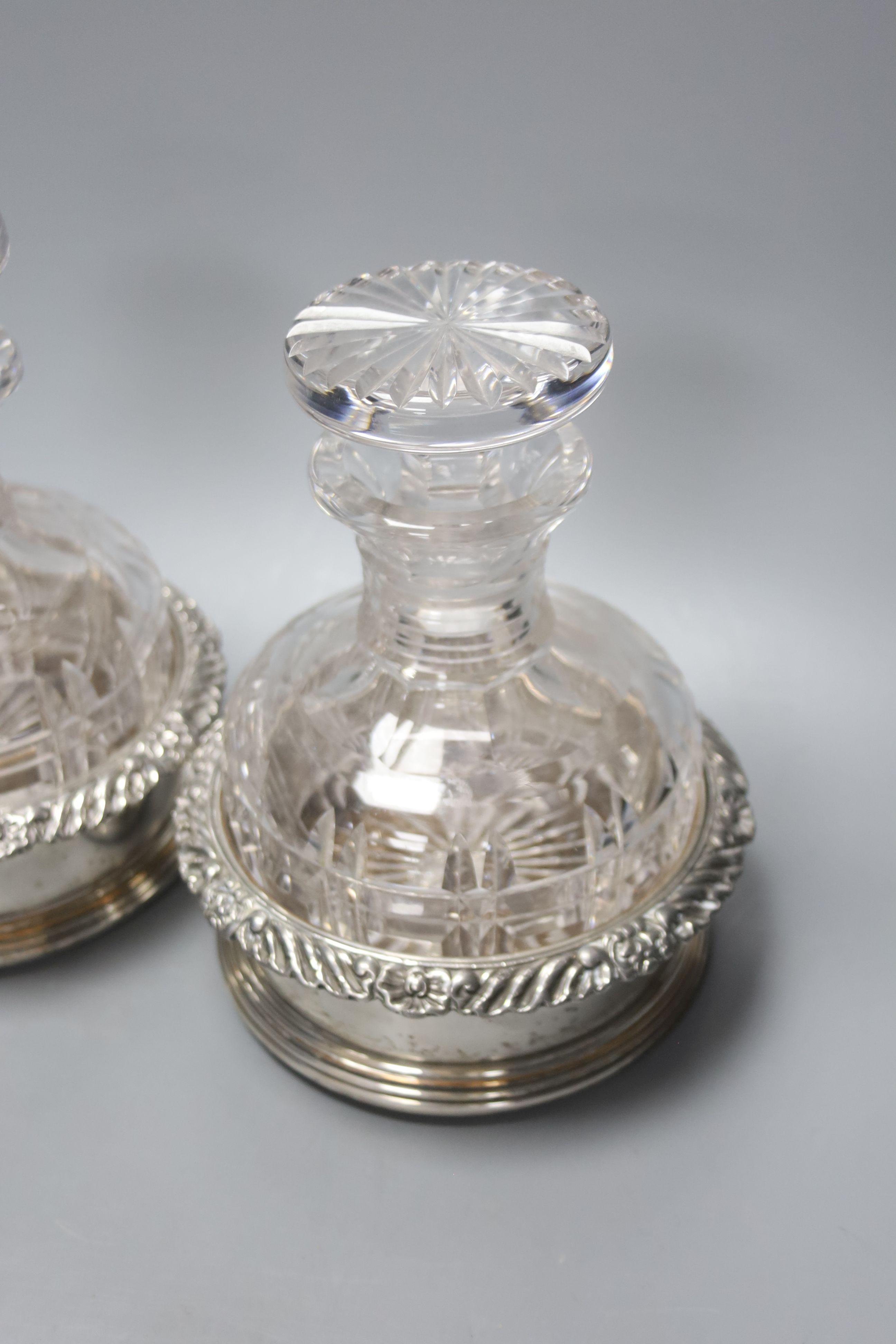A pair of silver plated coasters with cut glass decanters. 20cm